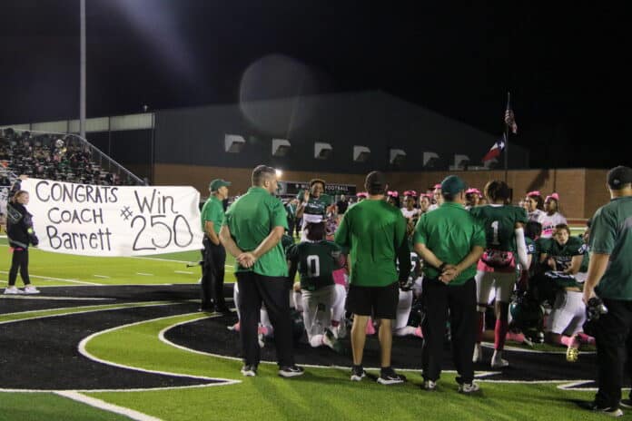 Coach Barrett and his team in front of a banner that is congratulating him on 250 wins.